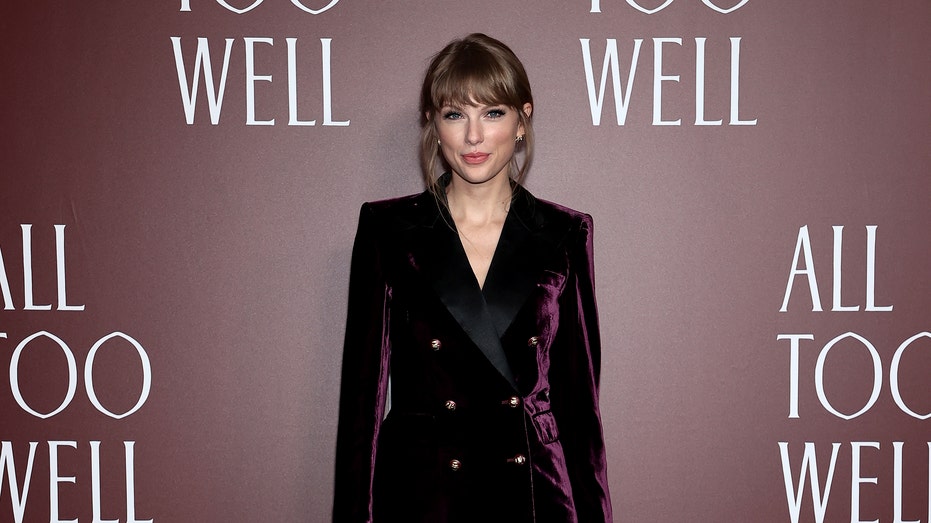 Taylor Swift smiles in a dark purple velvet matching two piece suit set