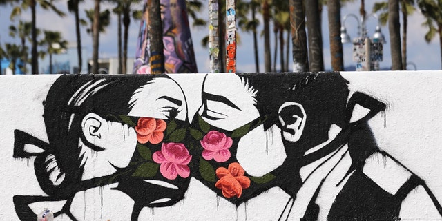 Palm trees stand behind a street art piece by artist Pony Wave depicting two people kissing while wearing face masks on Venice Beach on March 21, 2020, in Venice, California.