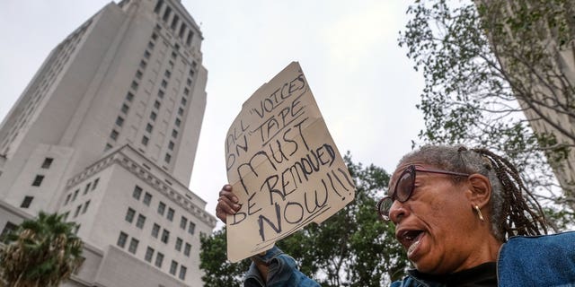 Veronica Sance holds a sign while denouncing racism and demanding change in response to a recorded, racially charged leaked conversation between leaders at City Hall and the Los Angeles County Federation of Labor President, before the Los Angeles City Council meeting outside City Hall Tuesday Oct. 11, 2022, in Los Angeles.